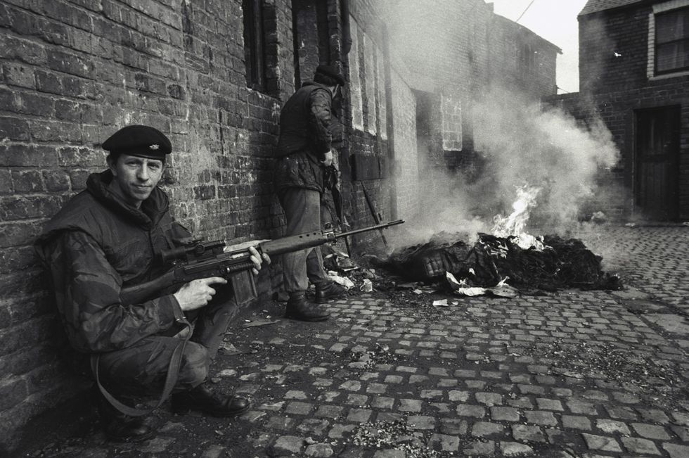 A British soldier provides cover for his fellow soldiers while they check out a burning building. The IRA was known to set fire to a building and wait for the soldiers to show up and then ambush them.