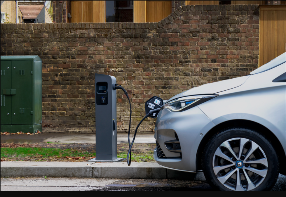 A BT electric vehicle charger with a green street cabinet in the background