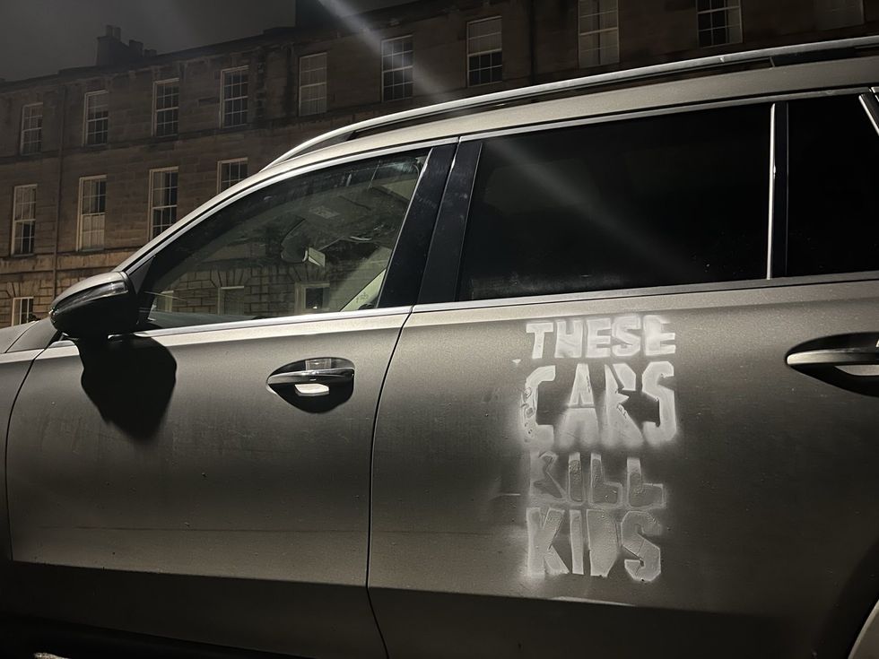 A defaced SUV with 'These cars kill kids' spray painted on the door