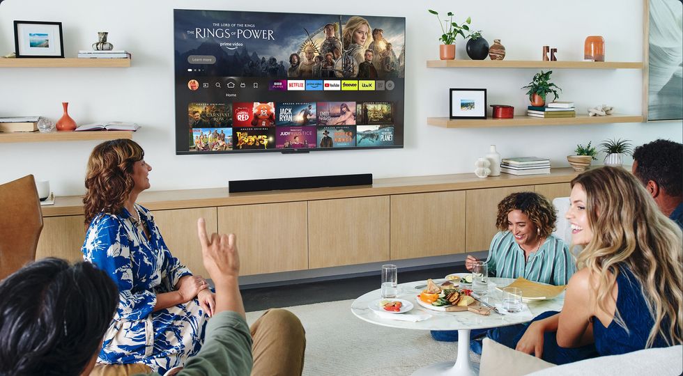 a group of people sit around a sofa watching an amazon fire tv omni series mounted on the wall