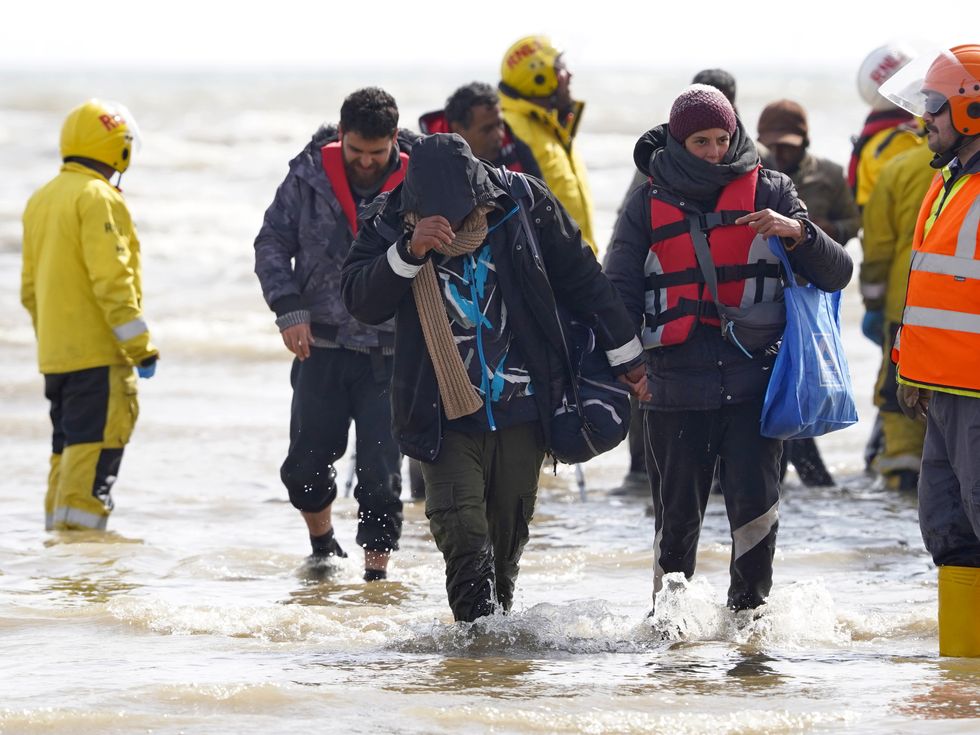 A group of people thought to be migrants are escorted up the beach in Dungeness, Kent