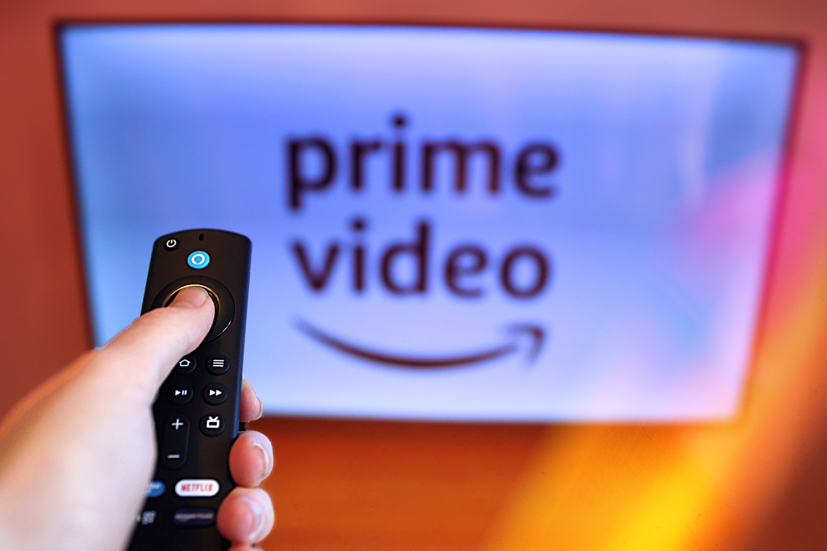 a hand holds a remote control in front of a television with the prime video logo on-screen 