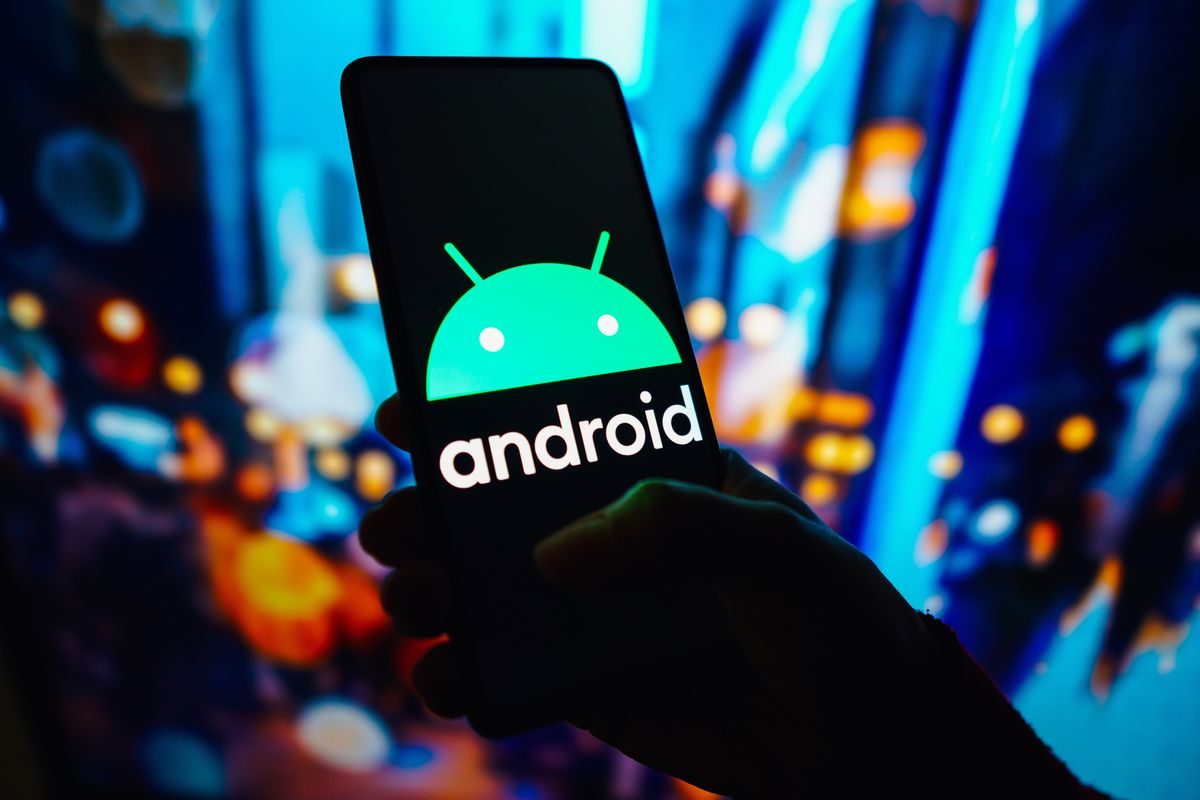 a hand holds a smartphone with the android operating system logo pictured on screen