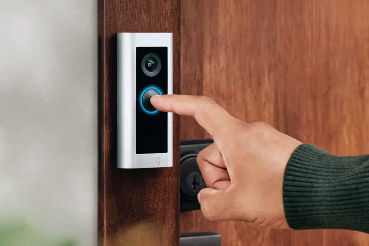 a hand is seen pressing a ring doorbell fitted to a wooden frame 