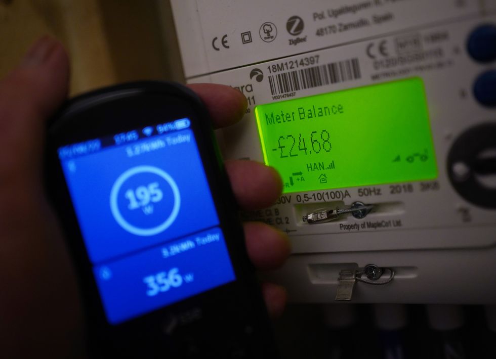 A handheld SSE smart meter for household energy usage is held next to an electricity meter.