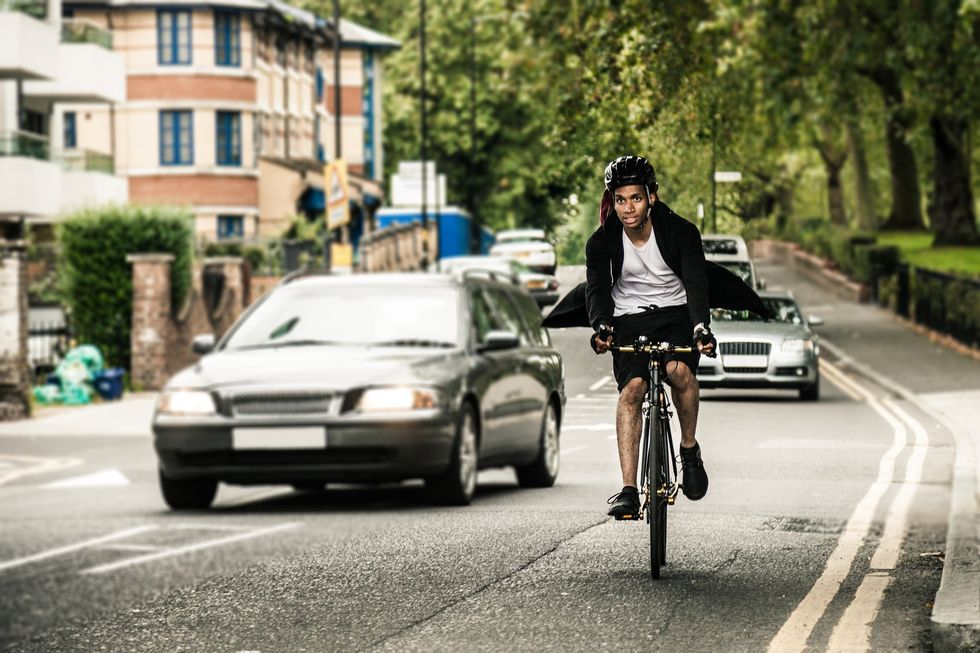 A man cycling on the road with cars in the background