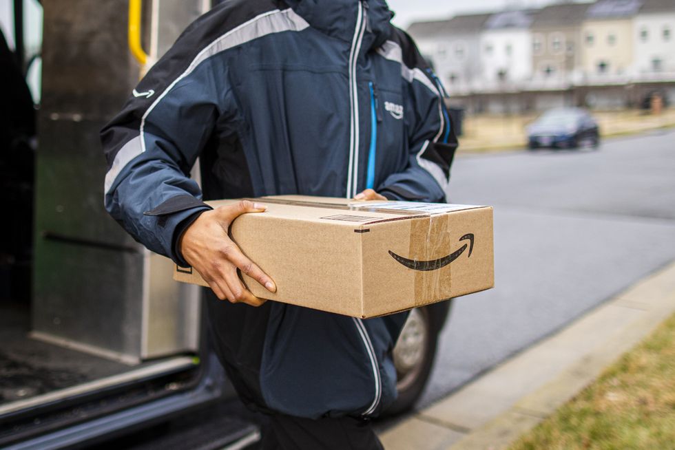 a man holds an amazon box with the prime logo as he walks out of a van 