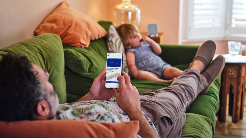 a man lying on the sofa checks the samsung smartthings app on her phone