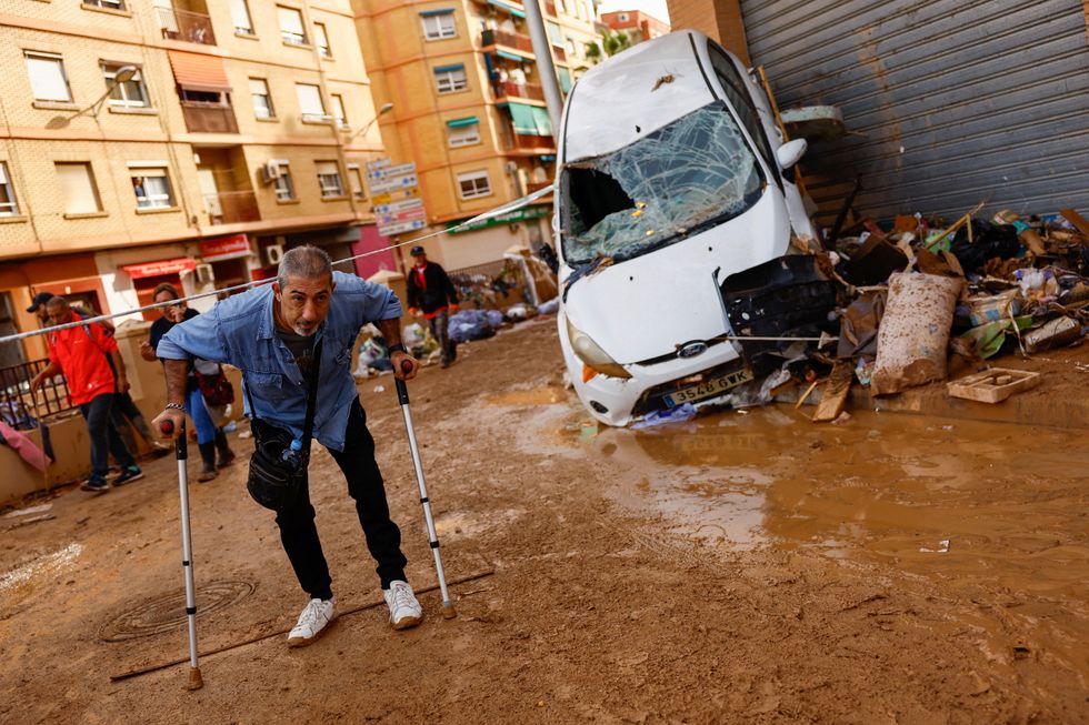 A man on crutches walks next to a damaged car, after heavy rains in Alfafar, in Valencia, Spain, November 1, 2024. REUTERS/Susana Vera