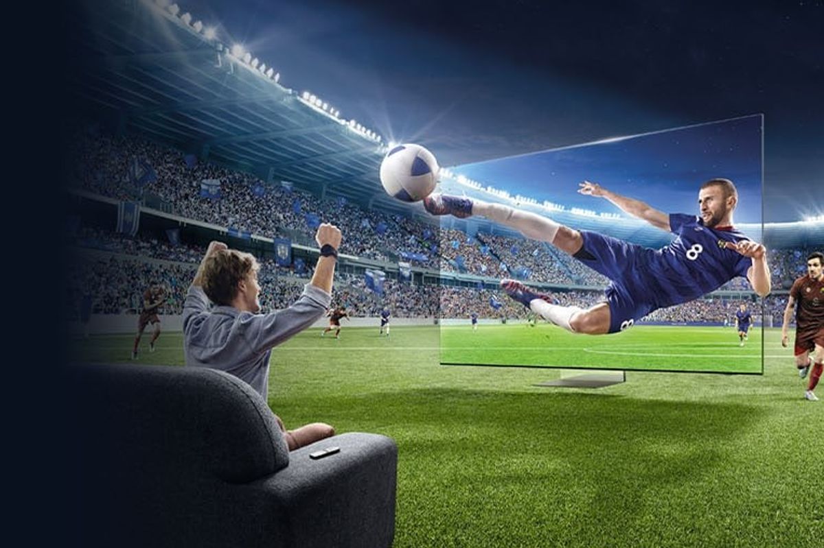 a man sits on the sofa cheering as a footballer emerges from a flatscreen samsung tv 