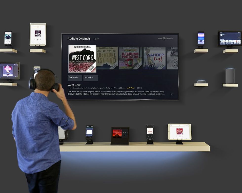 a man stands with a pair of headphones looking at a flatscreen television showing the audible interface