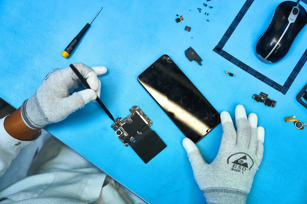 a pair of hands in gloves works on a smartphone from above, with components shown scattered around the table