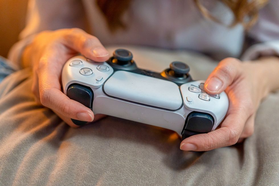 a pair of hands pictured holding a PlayStation 5 controller on a blanket   