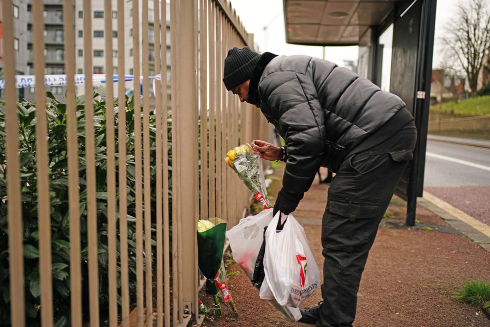 A person leaves flowers next to a bus stop on Woolwich Church Road