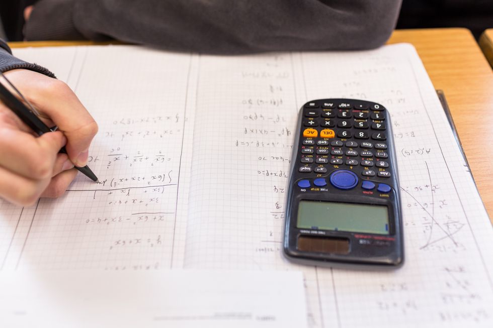 A person writing solving a math equation with a scientific calculator