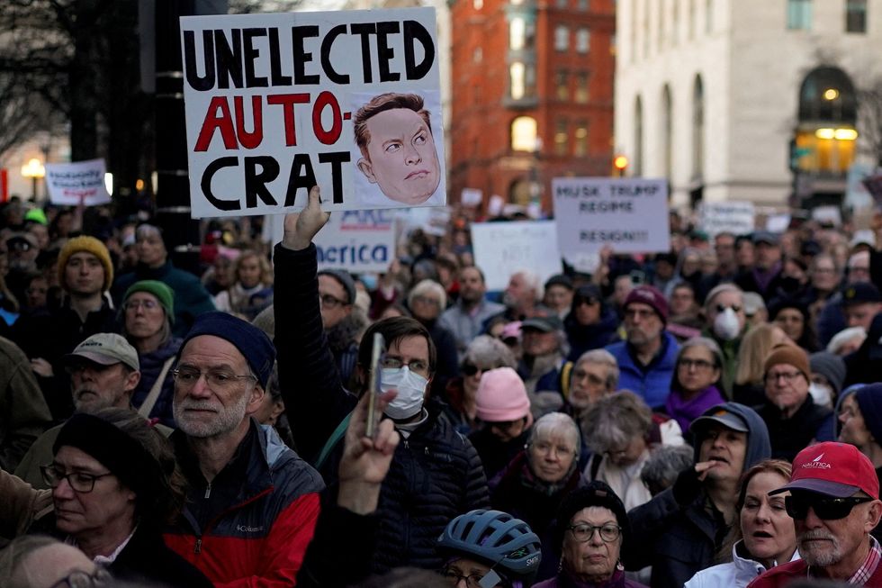 A protest against Elon Musk with a sign saying 'unelected auto-crat'