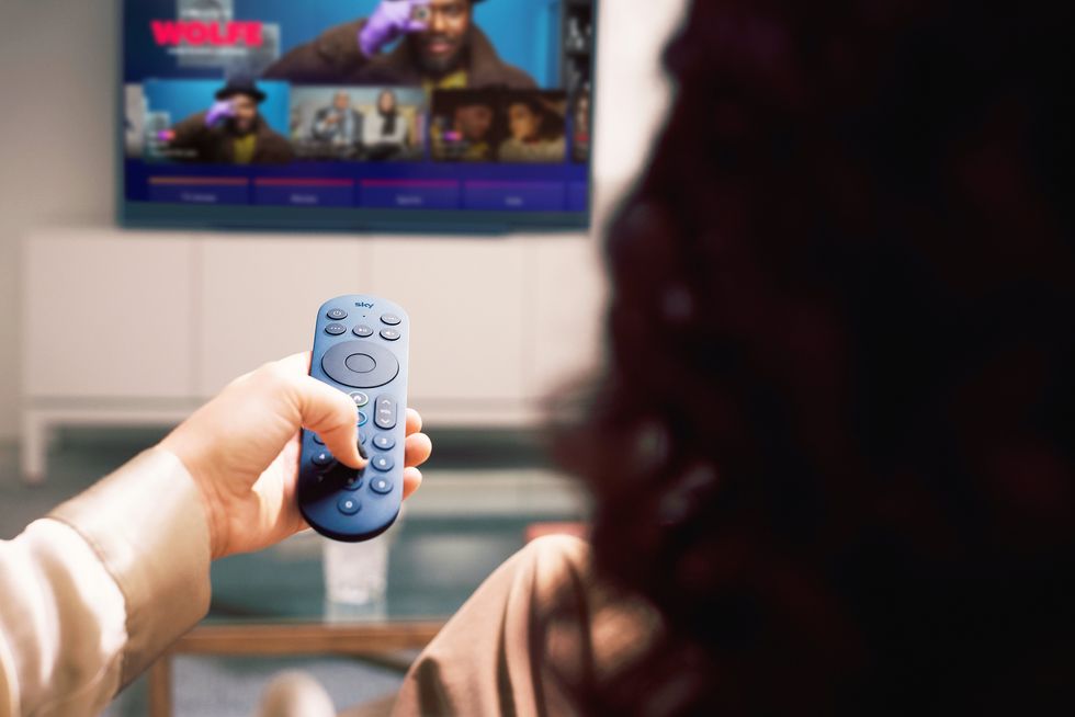 a woman holds a blue remote pointed at a sky glass television 