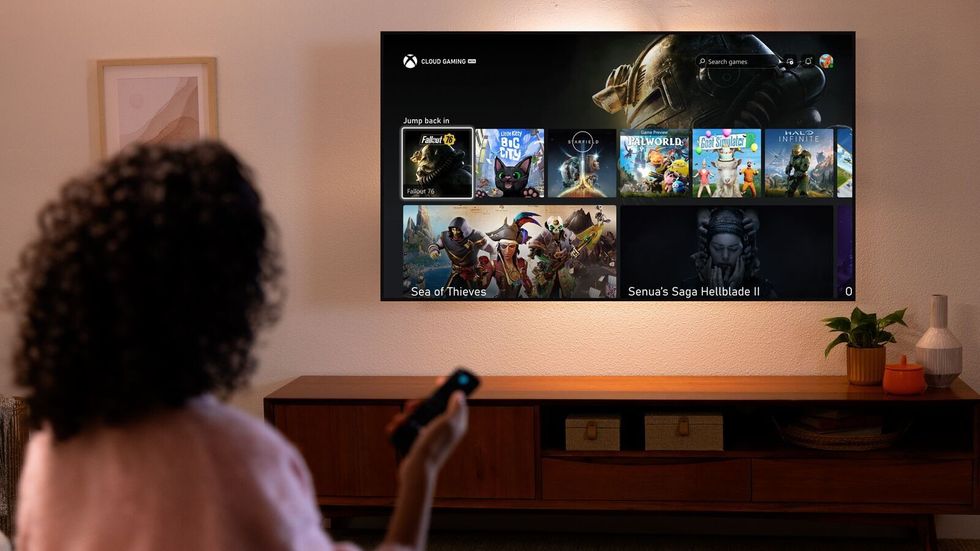 a woman holds a fire tv stcik remote with xbox games shown on-screen 