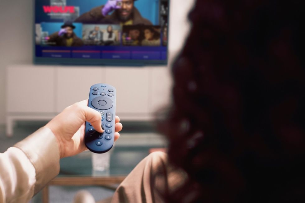 a woman holds out a blue sky glass remote control to change channels   