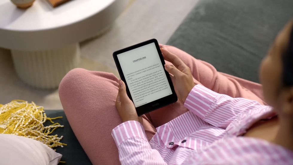 a woman sits and holds the 2024 kindle paperwhite to read