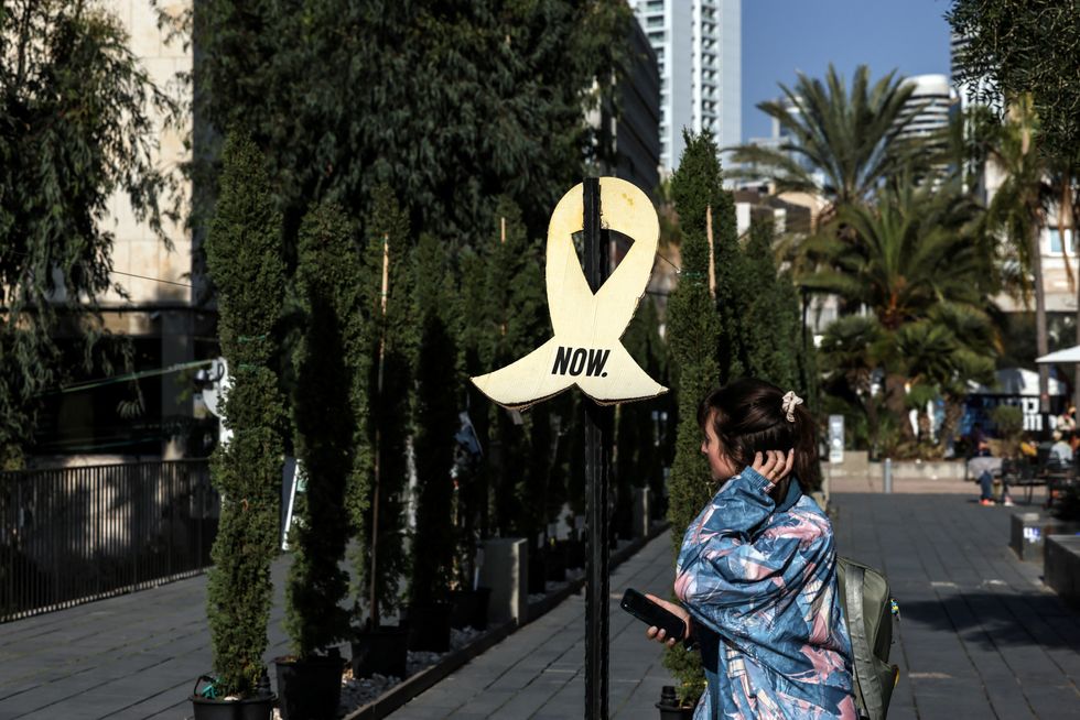 A woman walks next to a sign that symbolises the demand to release the hostages