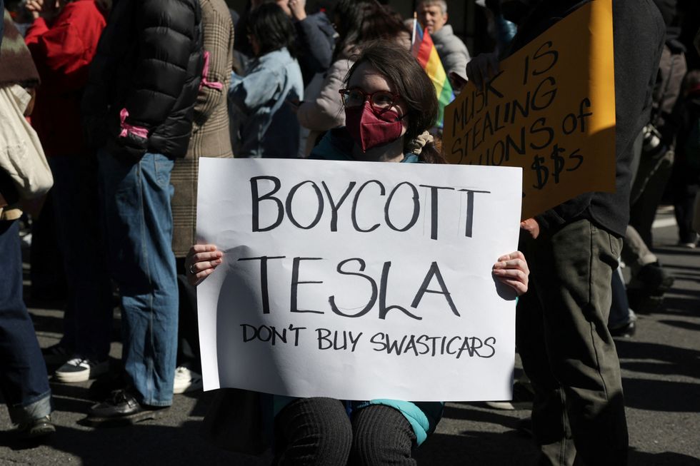 A woman with a 'Boycott Tesla: Don't buy Swasticars' sign