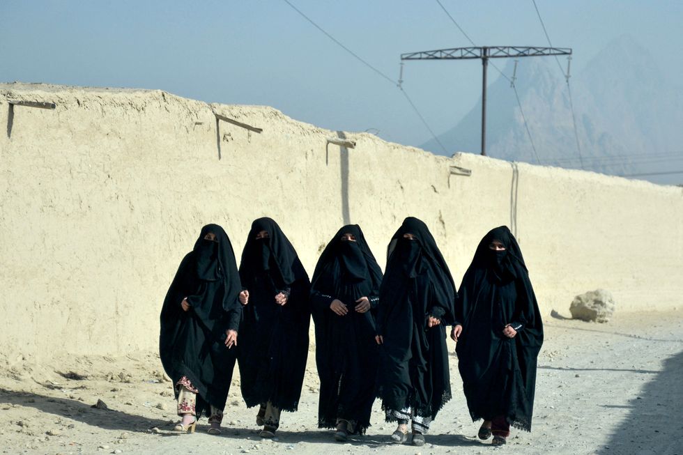 Afghan veiled women wearing abayas walk along a street in Kandahar on December 18, 2024