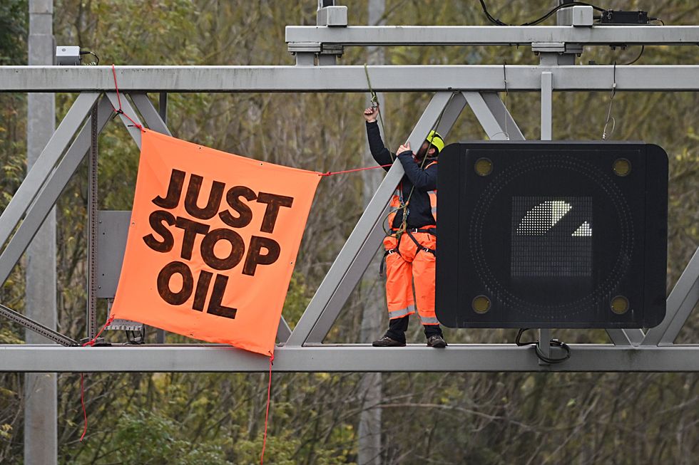 An activist puts up a banner reading "Just Stop Oil" atop an electronic traffic sign along M25 on November 10, 2022 i