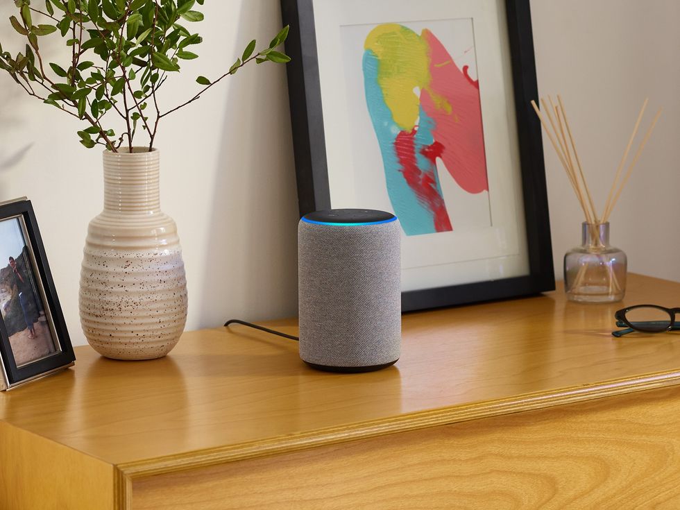 an amazon echo is pictured on a wooden cabinet with picture frames and flowers to the side 