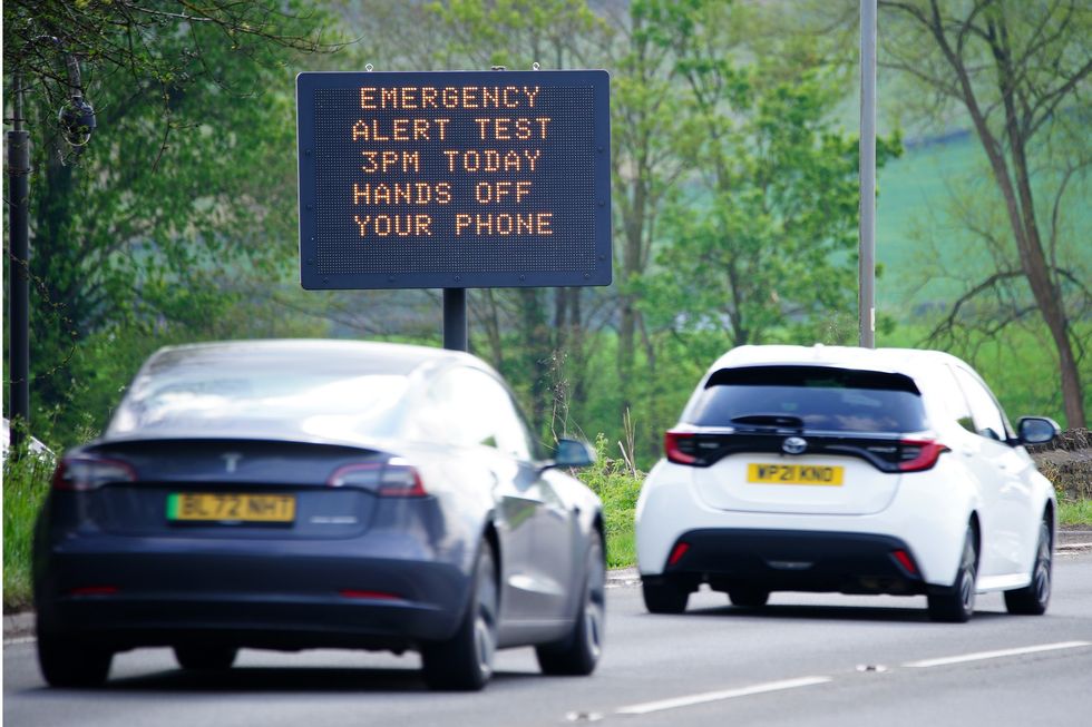 cars on uk road drive past a sign that reads emergency alert test 3pm today hands off your phone