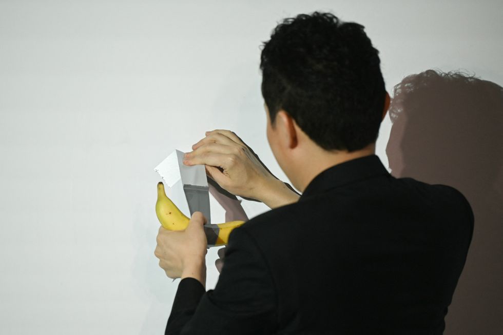 Chinese-born crypto founder Justin Sun prepares to eat a banana artwork composed of a fresh banana stuck to a wall with duct tape