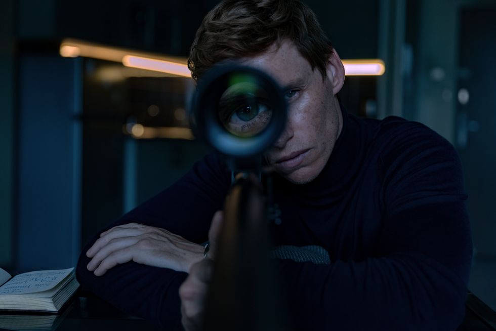 Eddie Redmayne pictured in black looking down the barrel of a gun