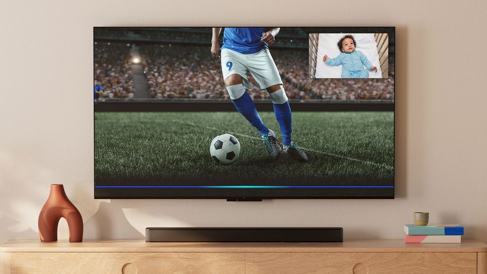 fire tv omni mini-led tv on the wall with a baby monitor video feed in the corner of a football match