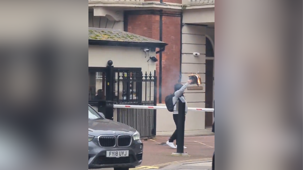 Footage shows a hooded man wearing a rucksack holding a book that has been set alight