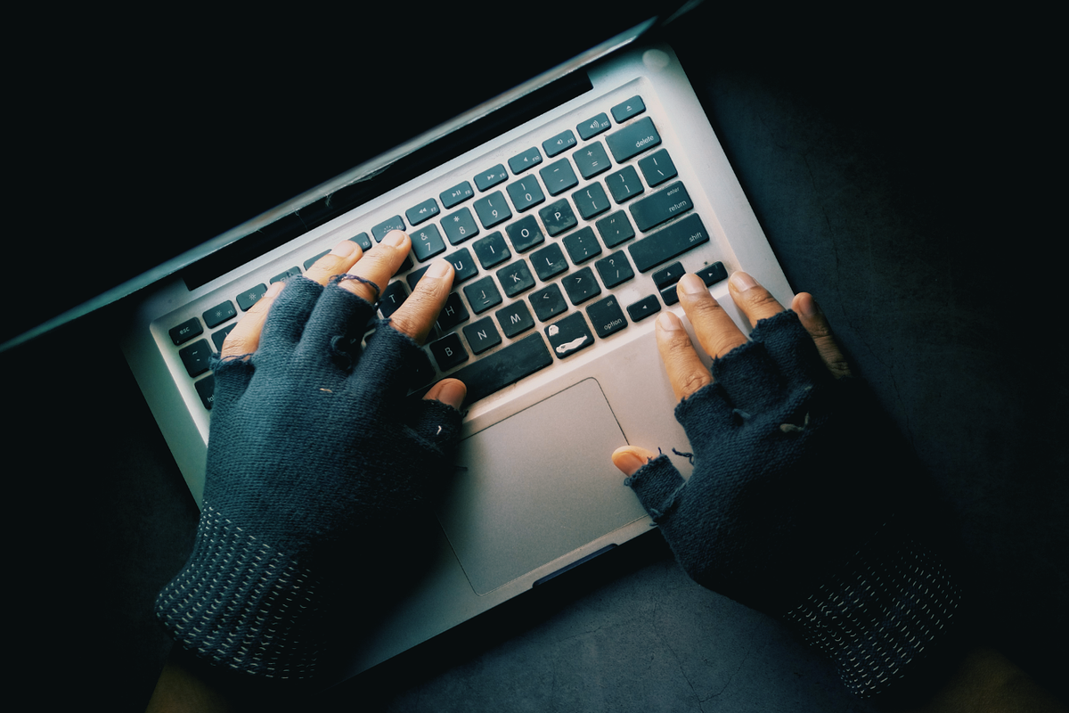 gloved hands pictured on the keyboard of a laptop typing in the dark 