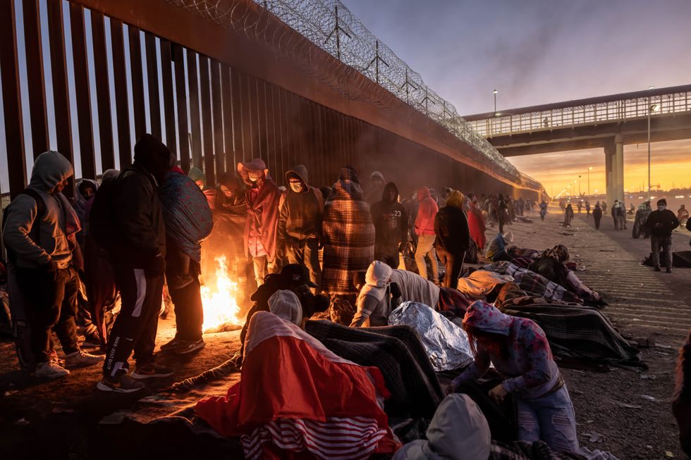 Immigrants keep warm by a fire at dawn after spending the night outside next to the U.S.-Mexico border fence on December 22, 2022 in El Paso, Texas