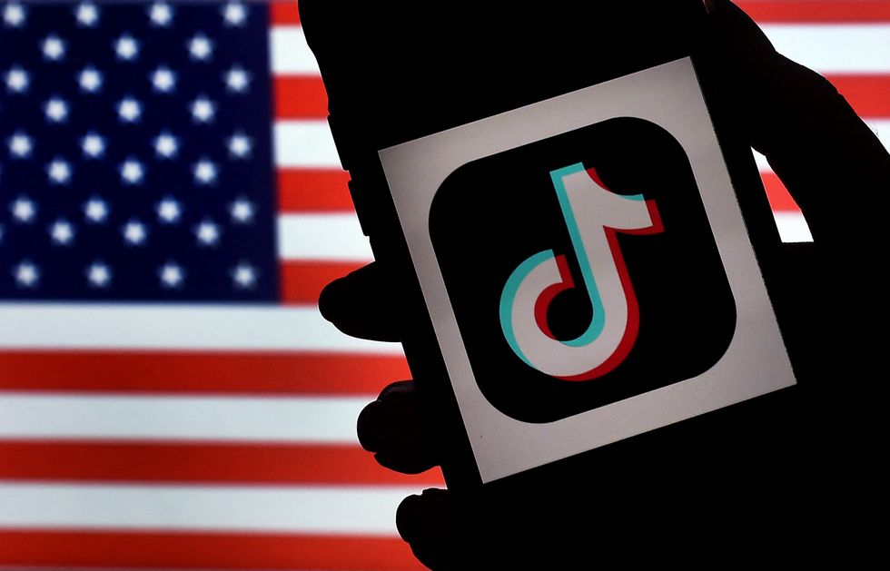 In this photo illustration, the social media application logo, TikTok is displayed on the screen of an iPhone on an American flag background