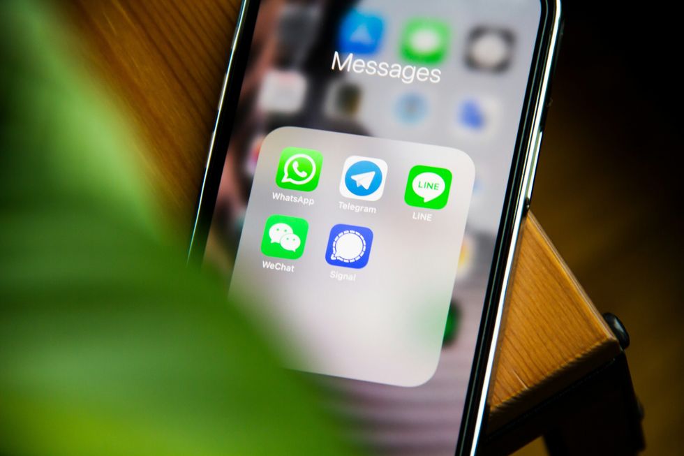 iphone placed on a table with a folder of messaging apps pictured on-screen 