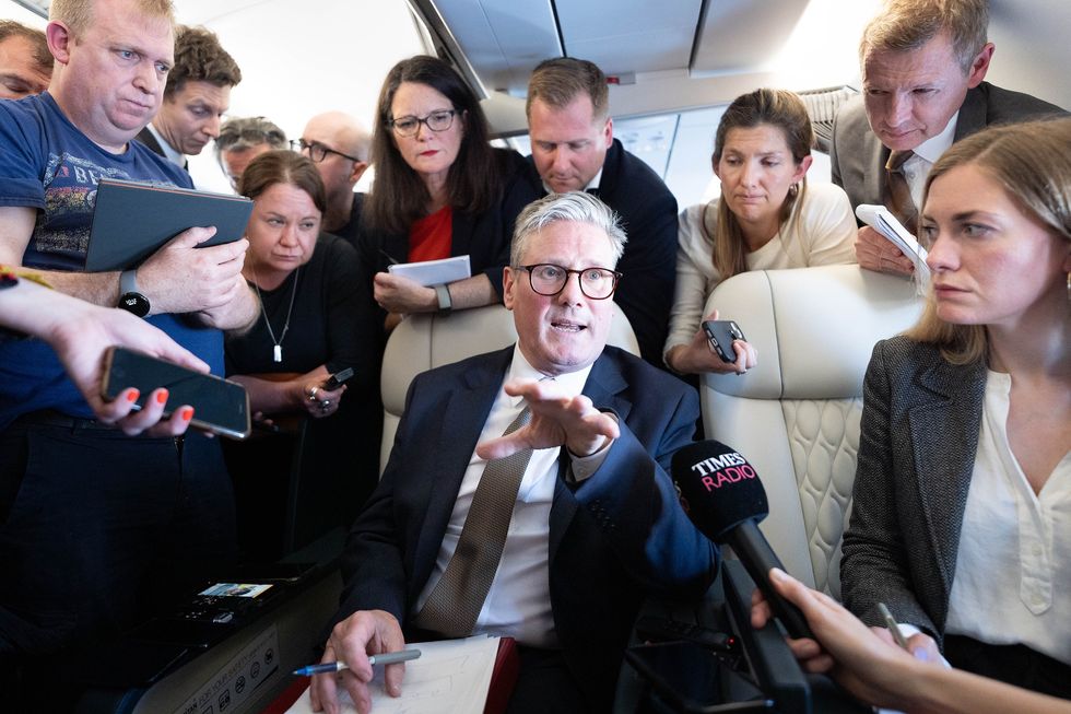 keir starmer pictured with a notebook and pen talking to journalists on a crowded plane