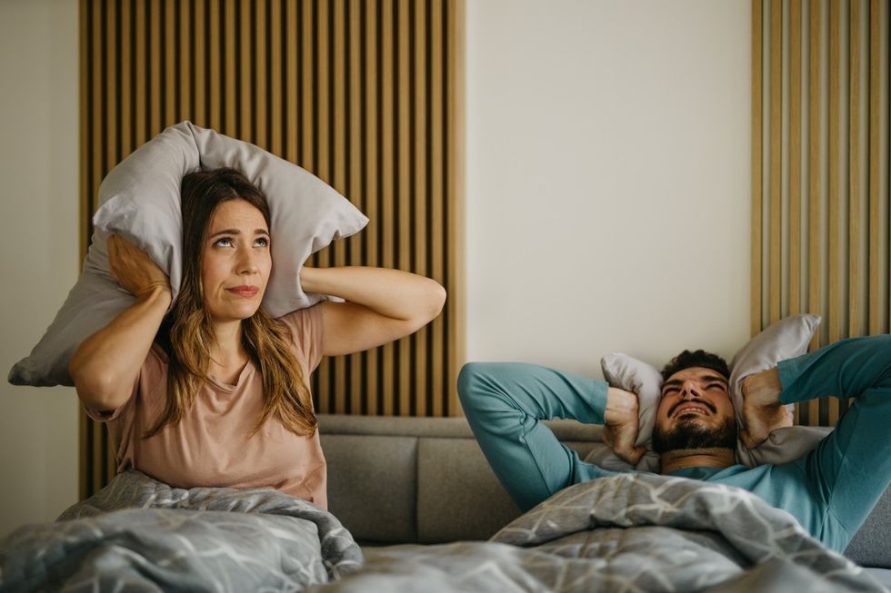 Man and woman cover ears with pillow due to noisy neighbours