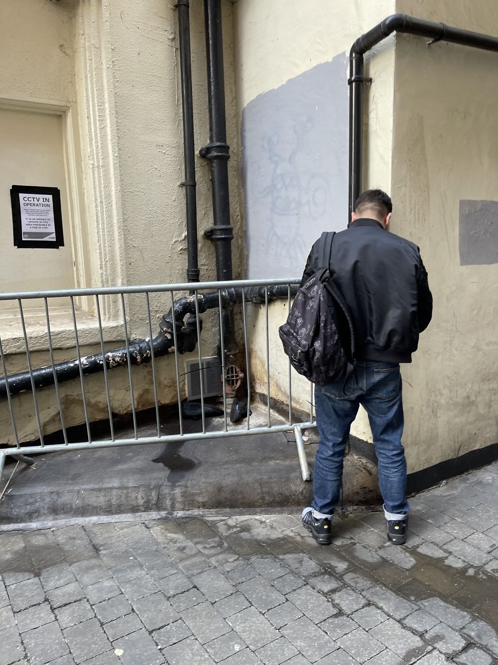 Man urinating next to sign telling him not to