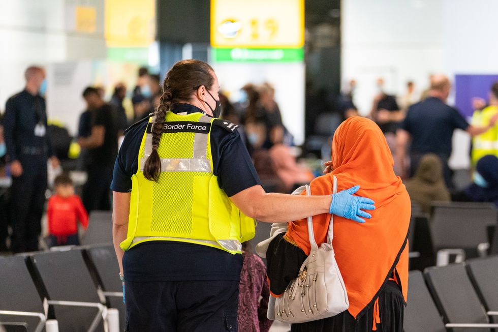 member of Border Force staff assists a female evacuee as refugees arrive from Afghanistan at Heathrow Airport on August 26, 2021 in London