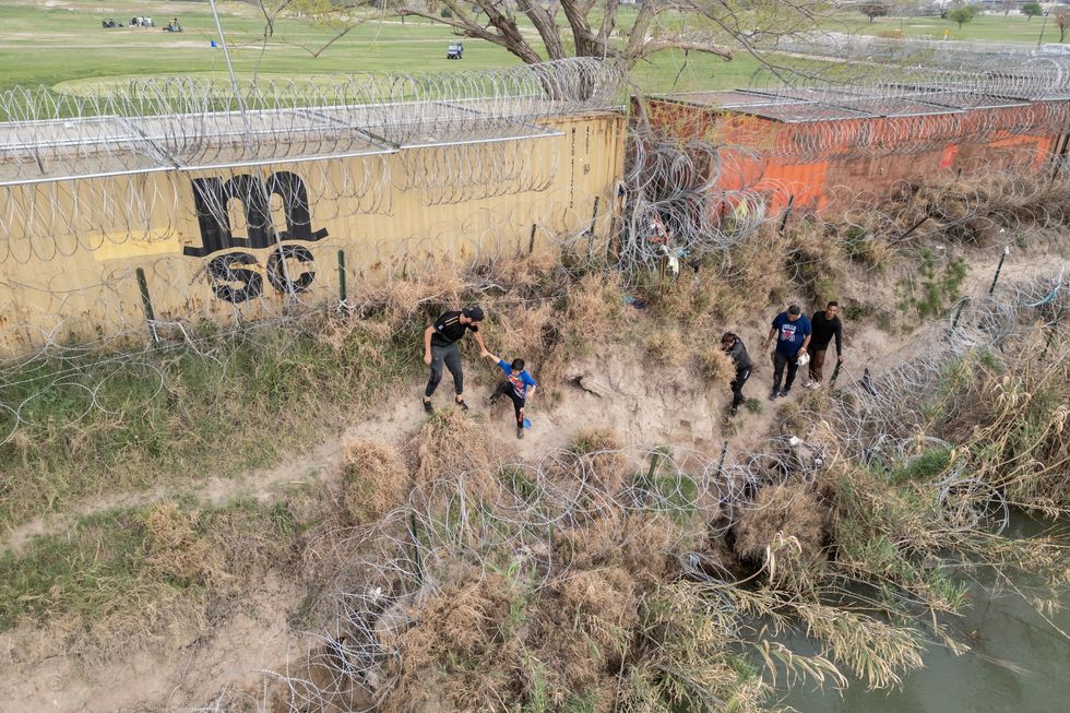 Migrants walk on the banks of the Rio Grande river