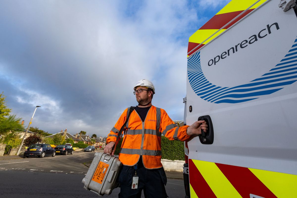 openreach engineer stands in a high-vis jacket with a box of tools outside of his van