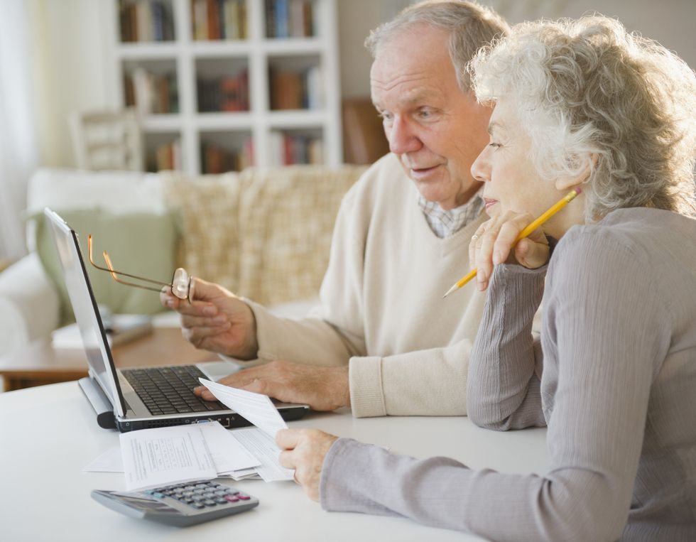 Pensioner couple look at finances on laptop with calculator beside them