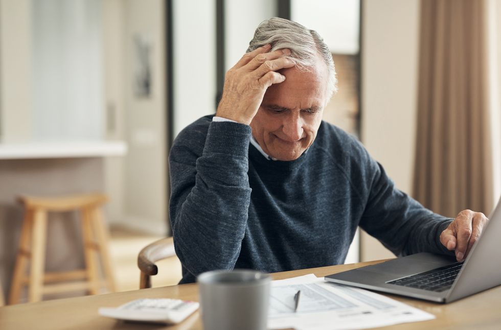 Pensioner looks worried at document beside laptop