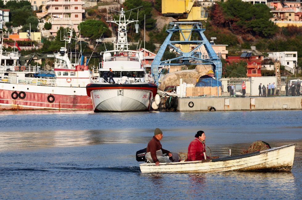 People on a fishing boat move past an Italian coast guard vessel that arrived to transfer migrants