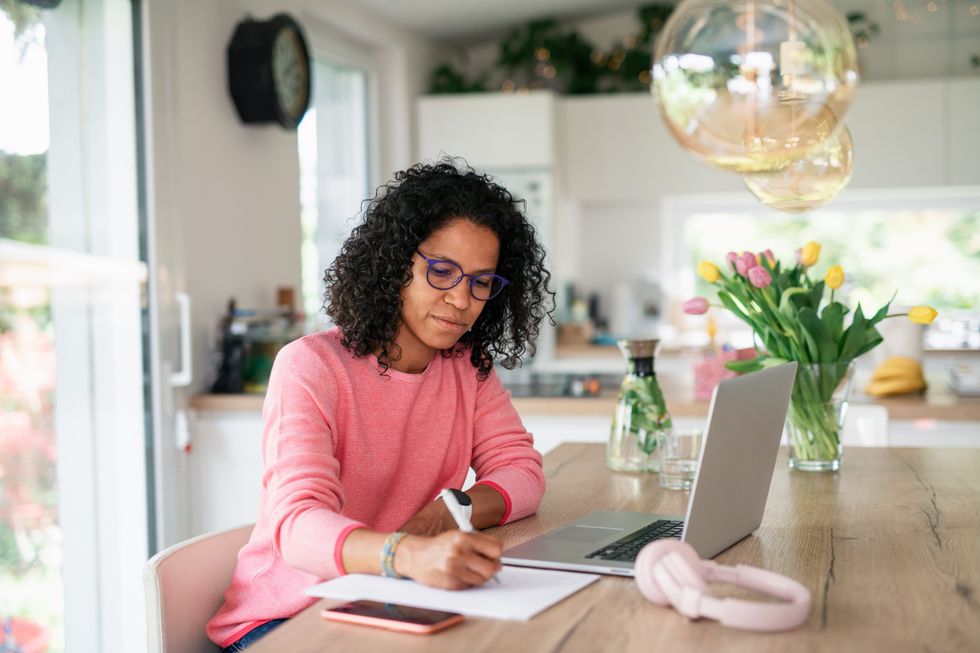 Person looks at notepad with laptop beside her