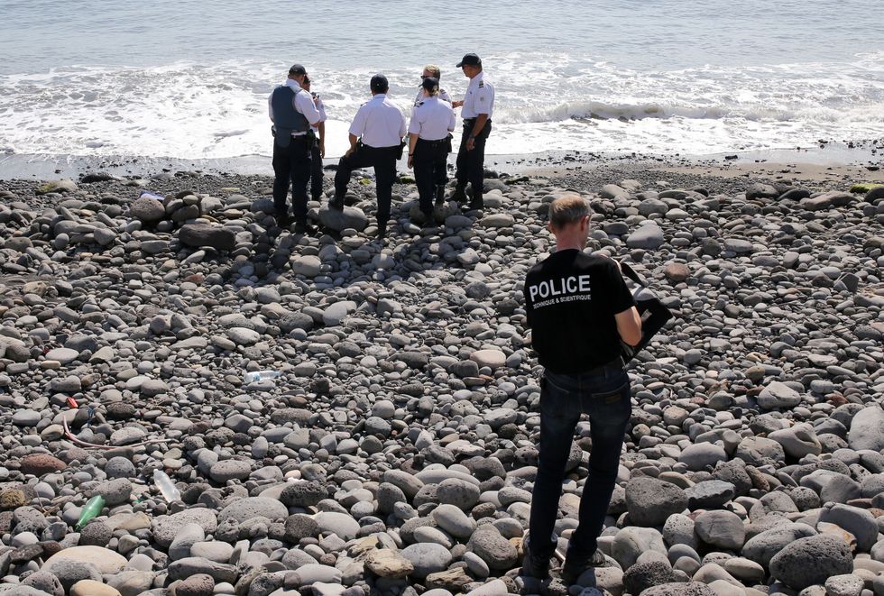 Police officers inspect metallic debris found on a beach in the search for MH370