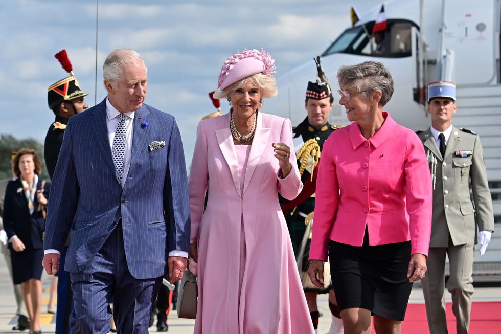 Queen Camilla fiercely holds onto hat as she looks pretty in pink